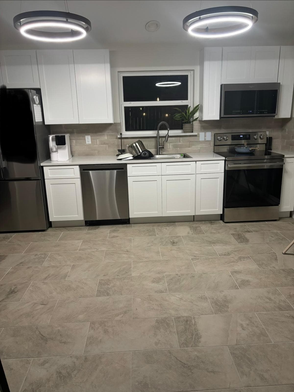 Completed kitchen remodel — white shaker cabinets, stainless appliances, new tile flooring and pendant lighting