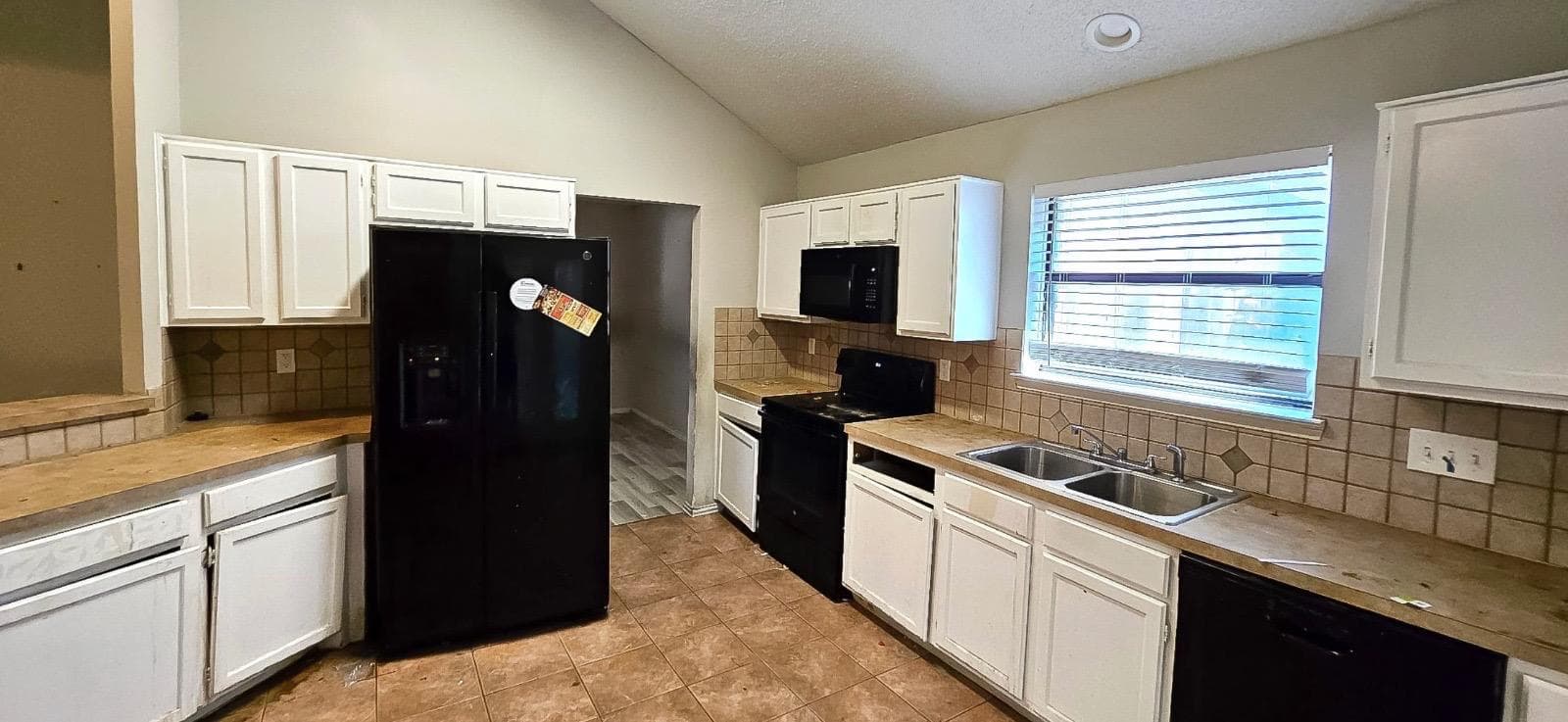 Kitchen before remodel — outdated black appliances, tile countertops, and dated cabinetry