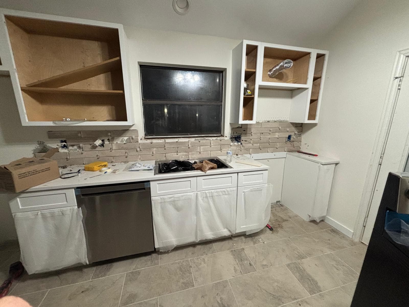 Kitchen remodel in progress — new cabinets installed, backsplash tile being set, appliances staged